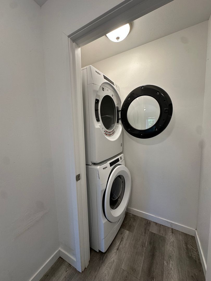 Stacked washer and dryer in a narrow laundry closet with a round mirror on the wall