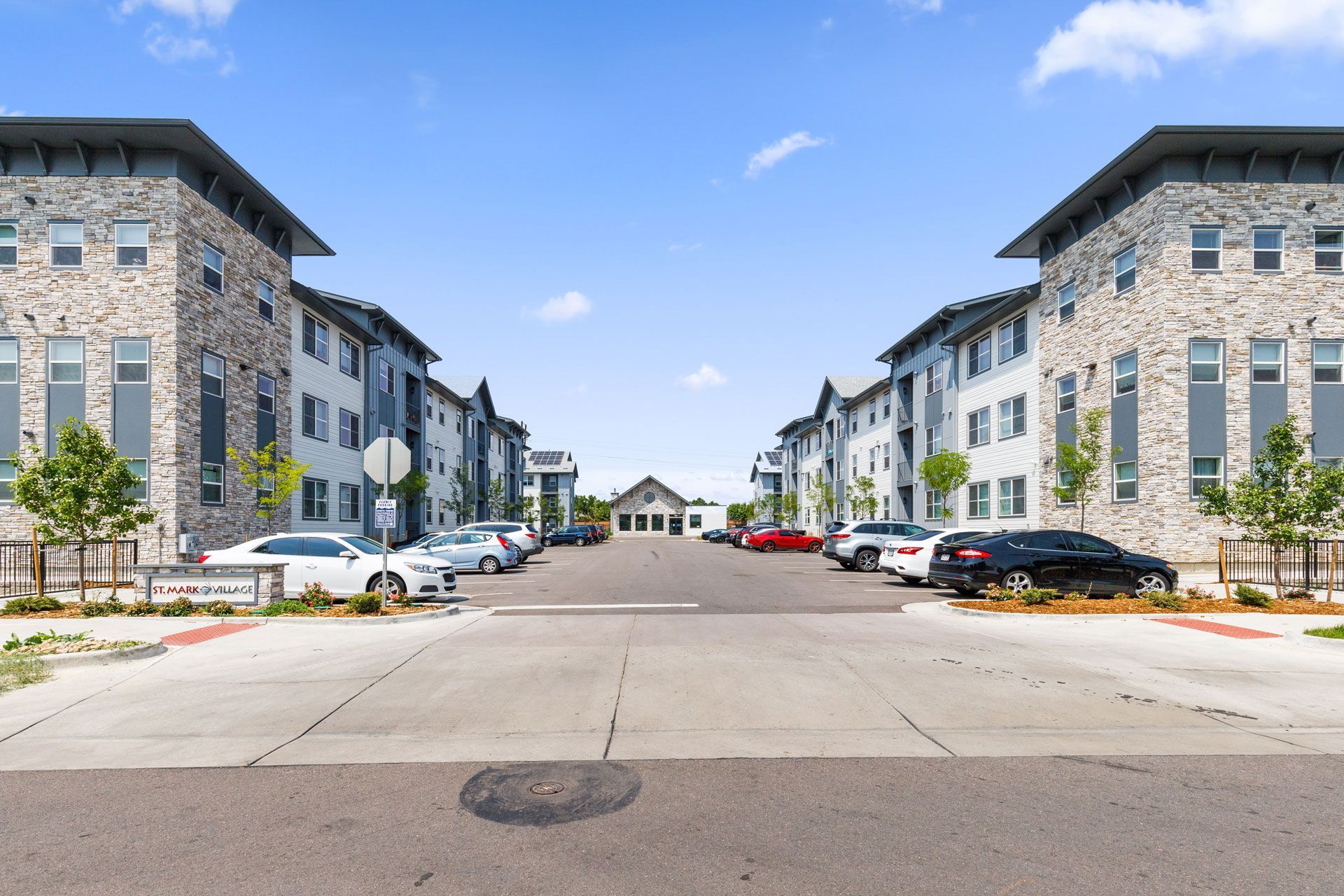 A street level view of a multi-story apartment complex with stone facades on either side of a paved parking area.