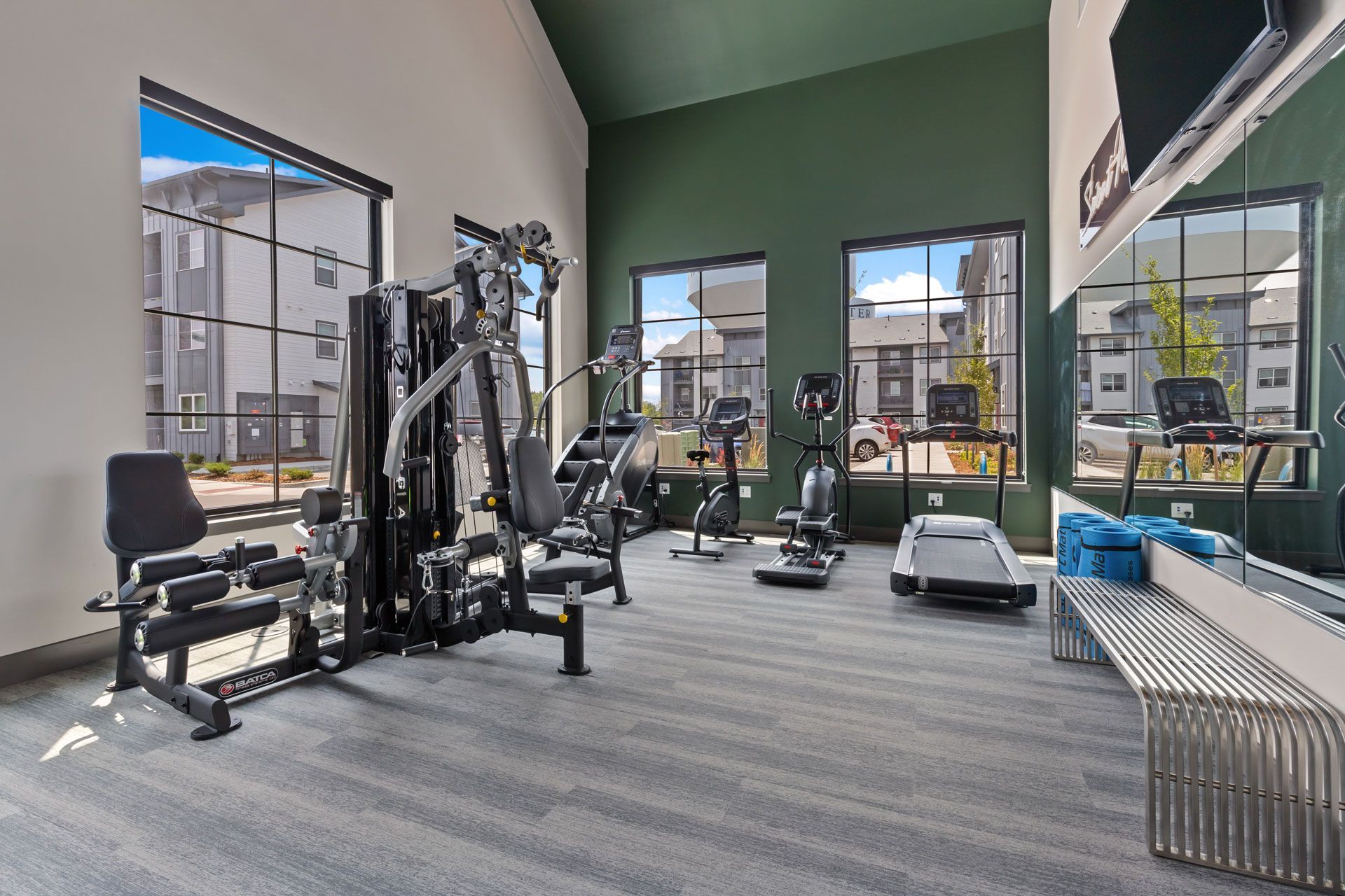 A modern fitness center featuring a multi-station weight machine, elliptical trainers, and treadmills on a gray carpet.