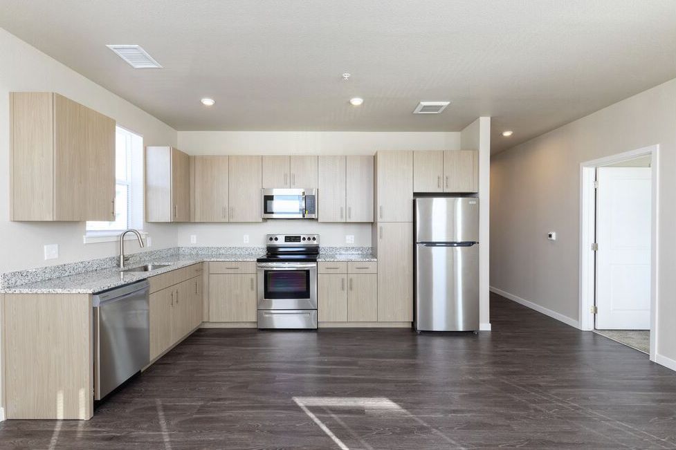 A modern kitchen with light wood cabinets, stainless steel appliances, granite countertops, and dark flooring.