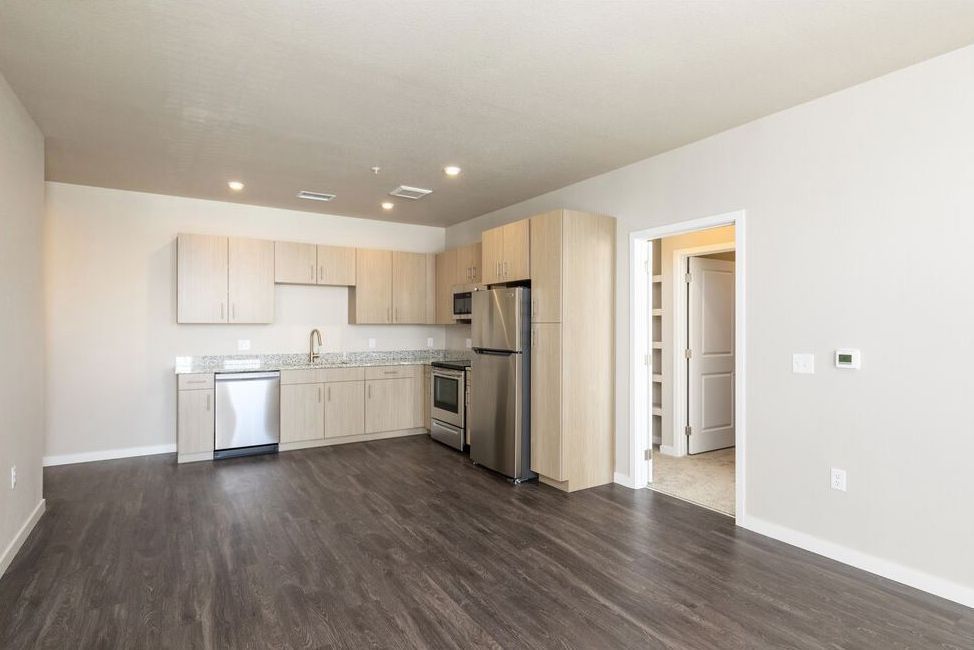 A modern, minimalist kitchen featuring light wood cabinets, stainless steel appliances, and wood-look flooring.