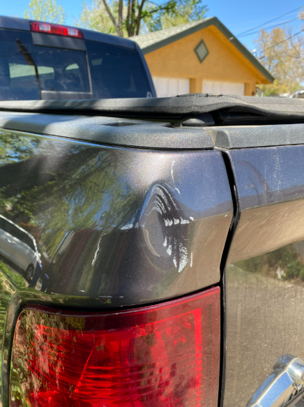 Close-up of a black pickup truck’s rear corner with a dented taillight panel in a driveway.