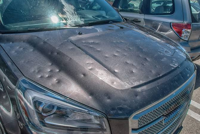 Close-up of a black car hood covered in water droplets in a parking lot