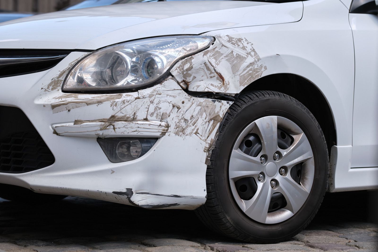 White car front end with heavy mud and damage near the bumper and wheel