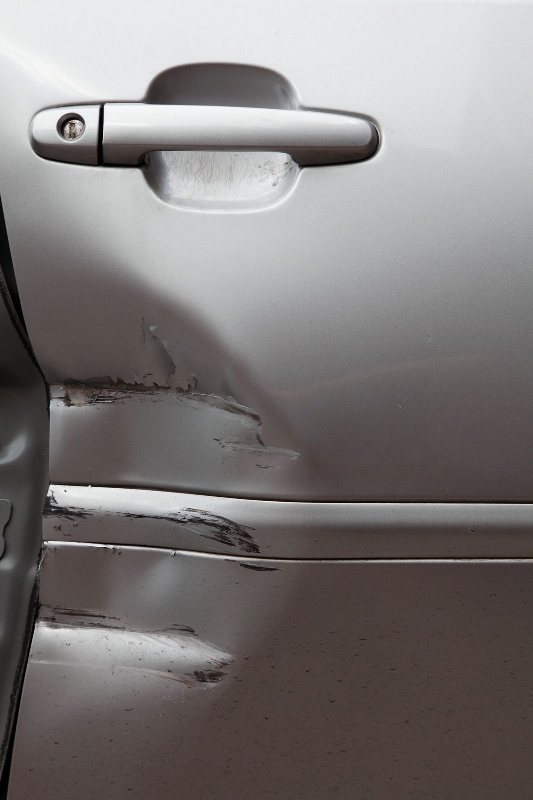 Close-up of a silver car door with visible dents and scratches near the handle.