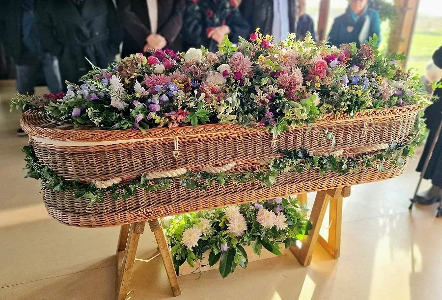 Red roses rest on a dark, reflective coffin.