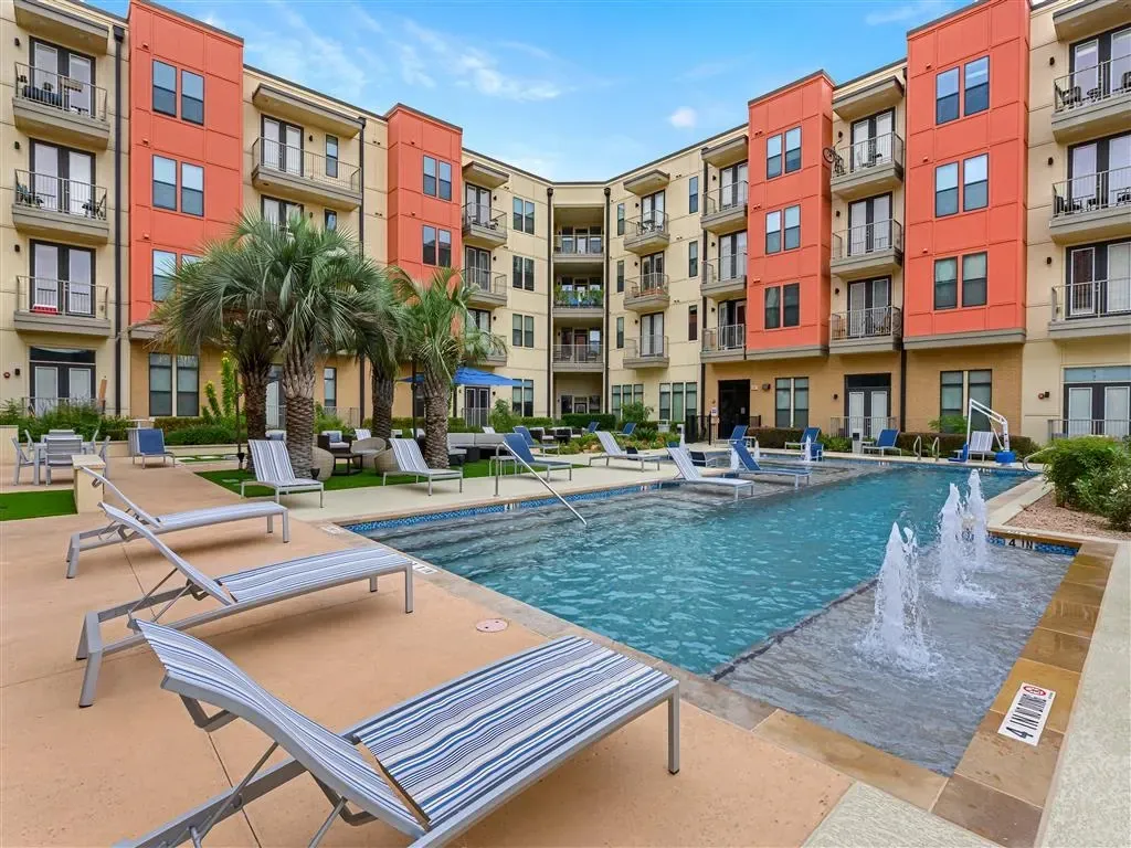 Modern apartment building with a sparkling blue swimming pool and lounge chairs.