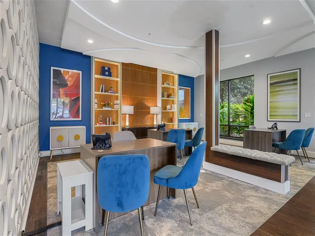 Reception desk with blue chairs in a modern leasing office with artwork and large windows.