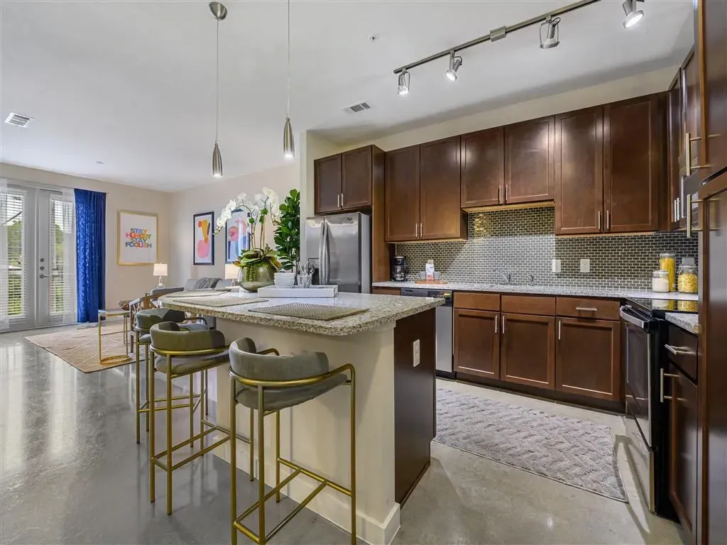 Modern kitchen with island and bar stools, connected to living area.