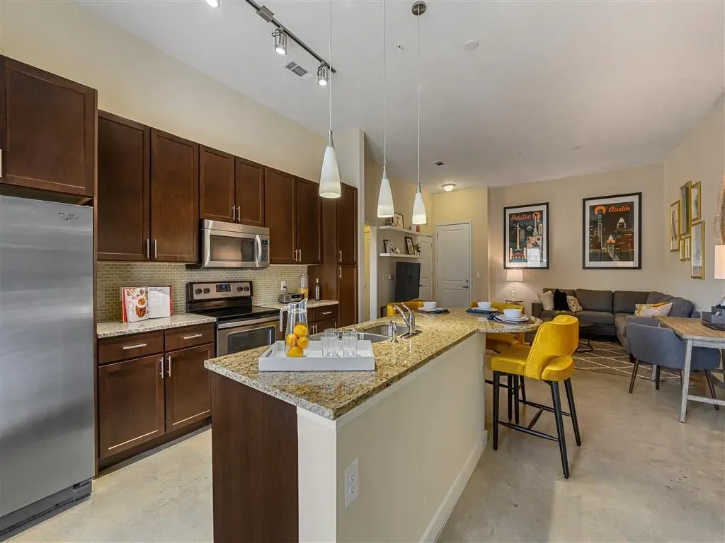 Modern apartment kitchen with dark wood cabinets, granite countertops, stainless steel appliances, and a breakfast bar with yellow stools.