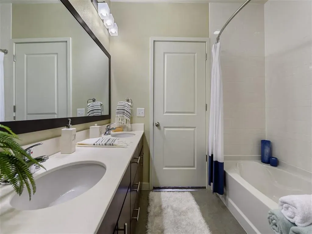 Double vanity bathroom with a large mirror, soaking tub, and white tiled shower.