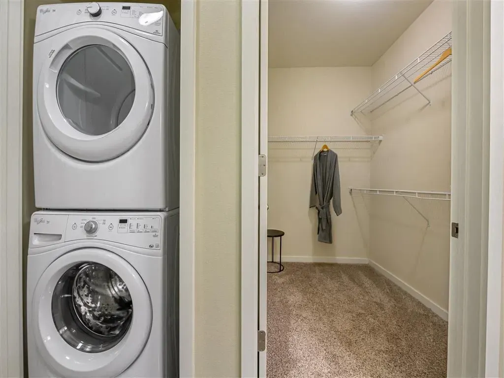 Stackable washer and dryer next to a walk-in closet with a bathrobe.