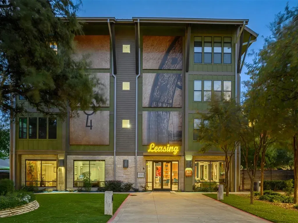 Modern apartment building exterior with a welcoming entrance and leasing office, surrounded by greenery and trees.