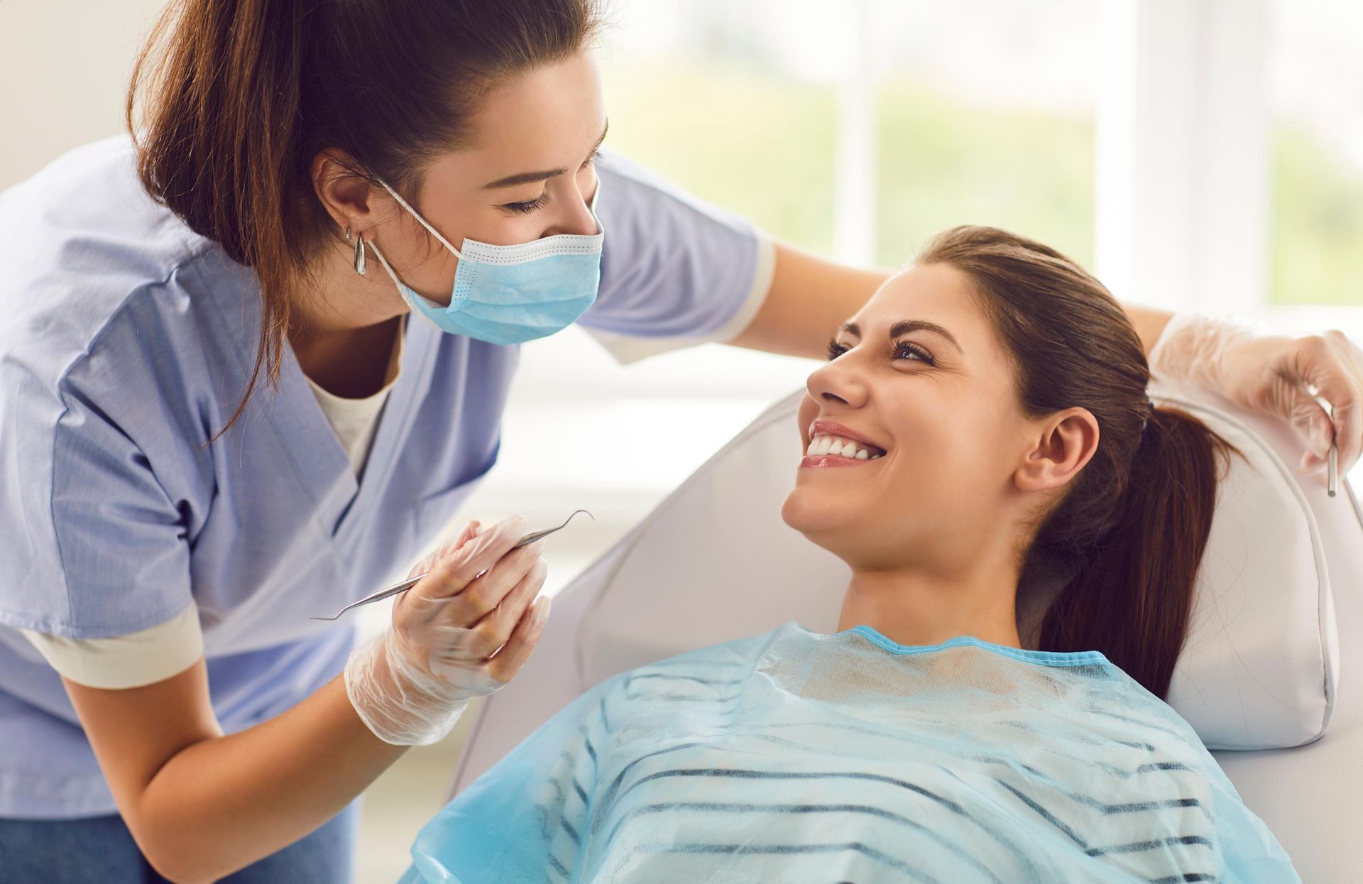 A woman is sitting in a dental chair while a dentist examines her teeth.