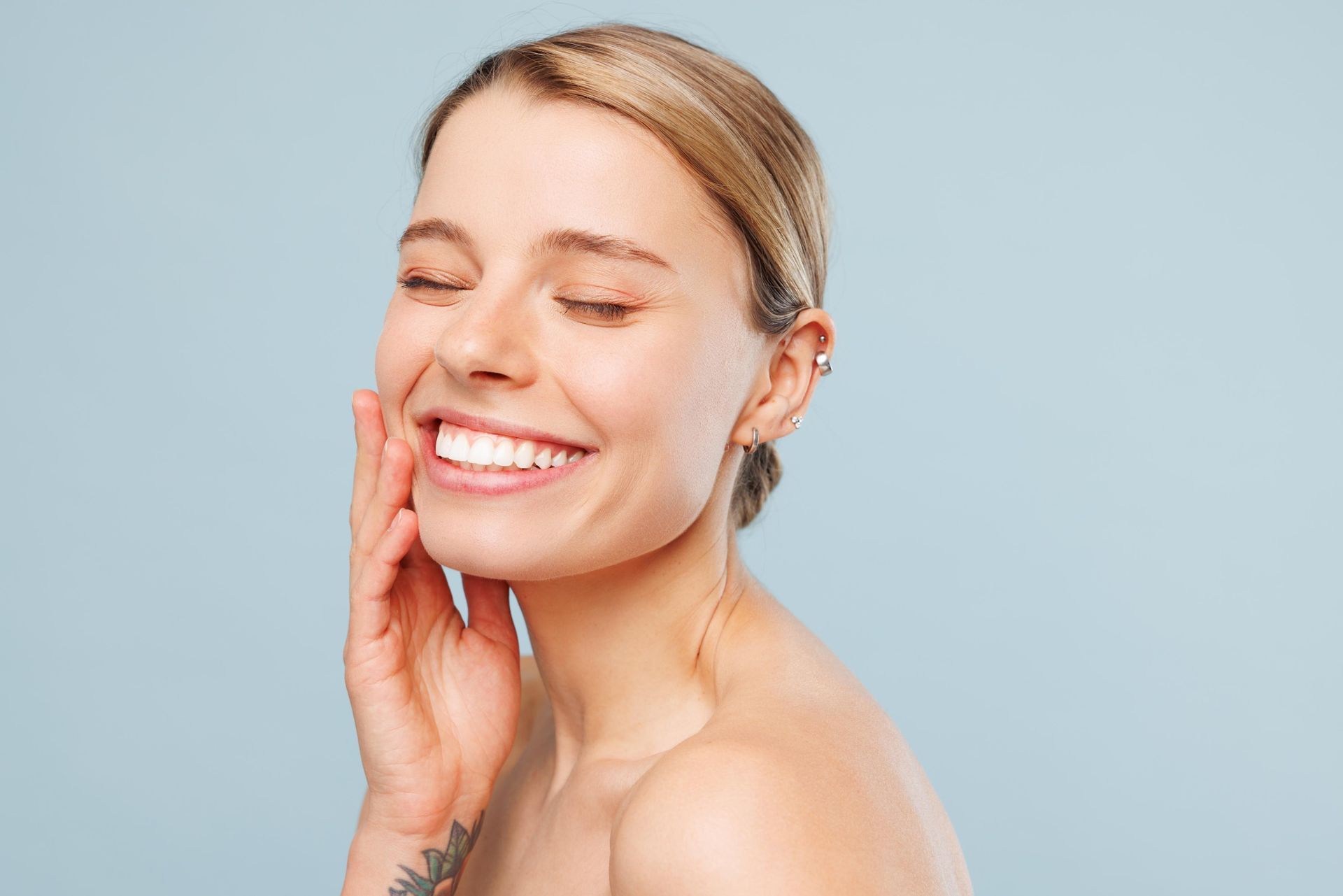 A woman is smiling and touching her face.