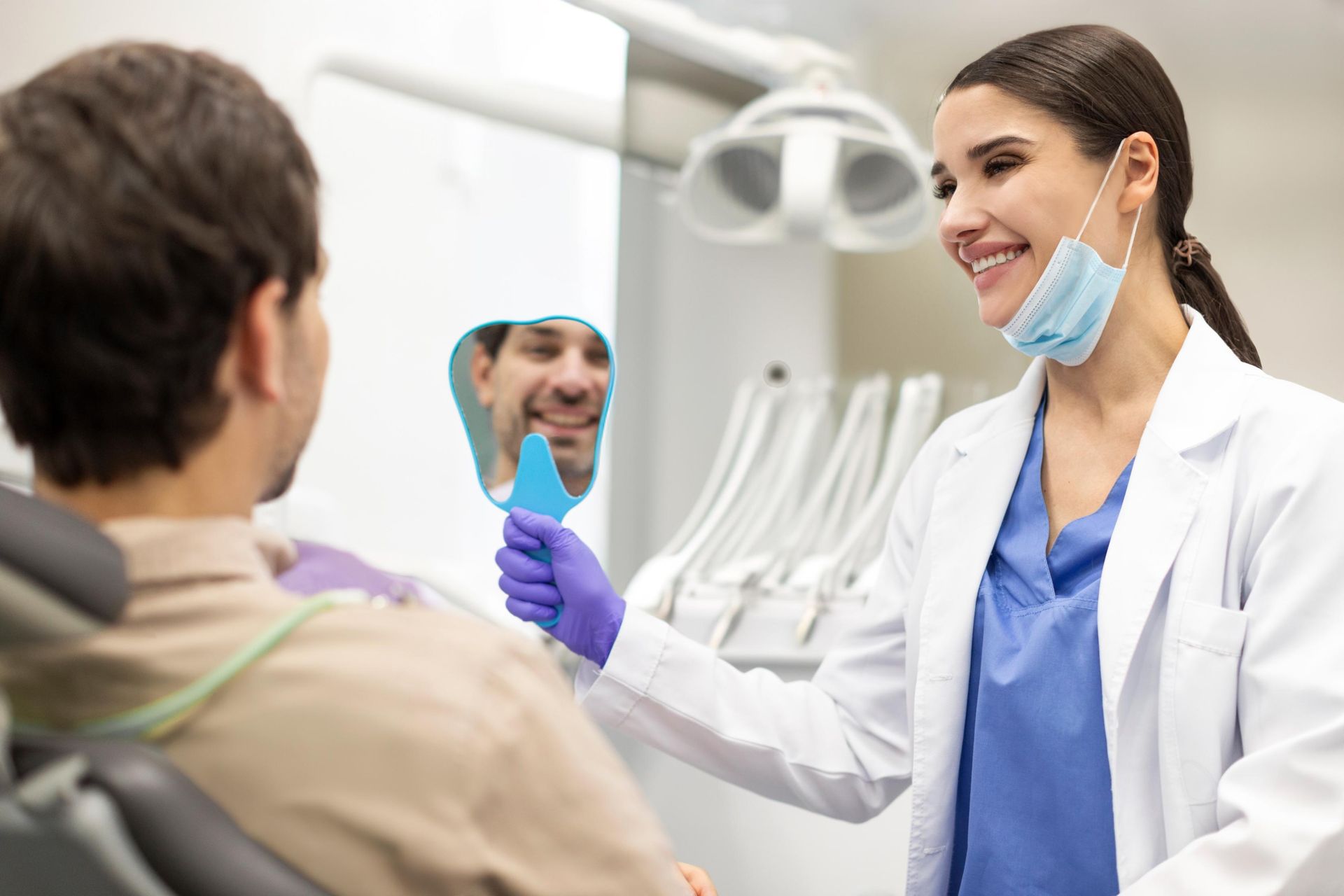 A dentist is looking at a patient 's smile in a mirror.