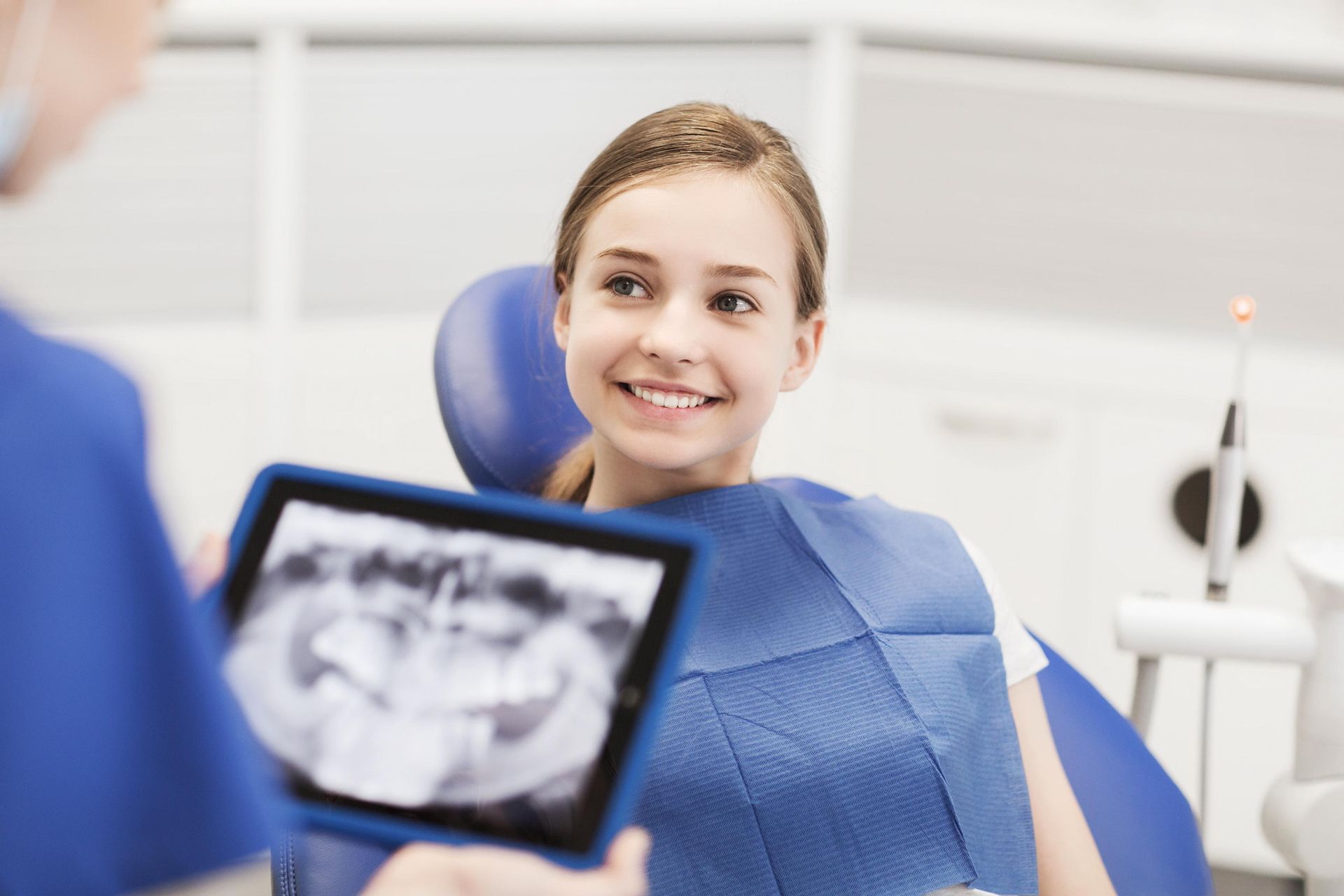 A young girl is sitting in a dental chair looking at an x-ray of her teeth.