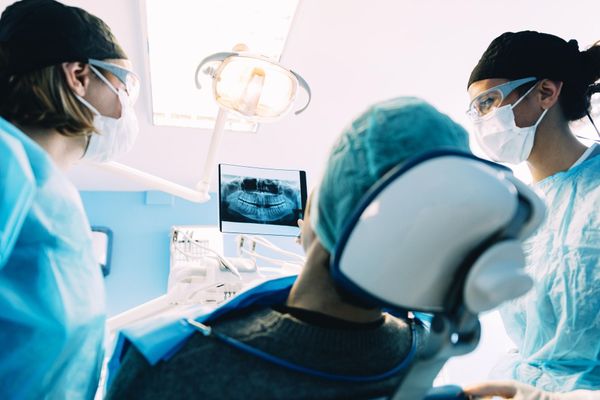 Two dentists are examining a patient 's teeth in a dental office.