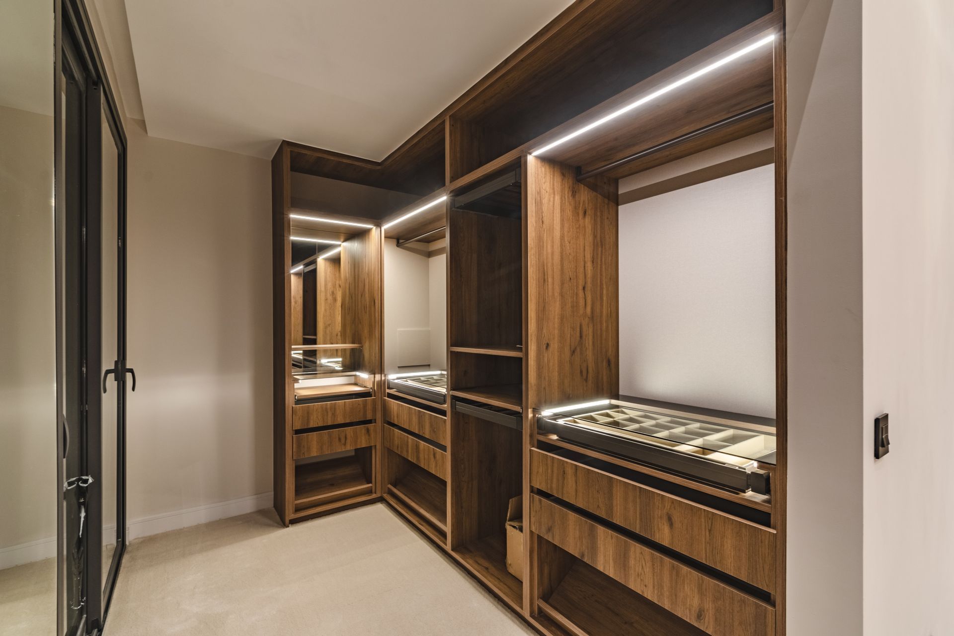 Luxury walk-in closet with wood cabinetry, glass-front drawers, mirrors, and warm LED lighting