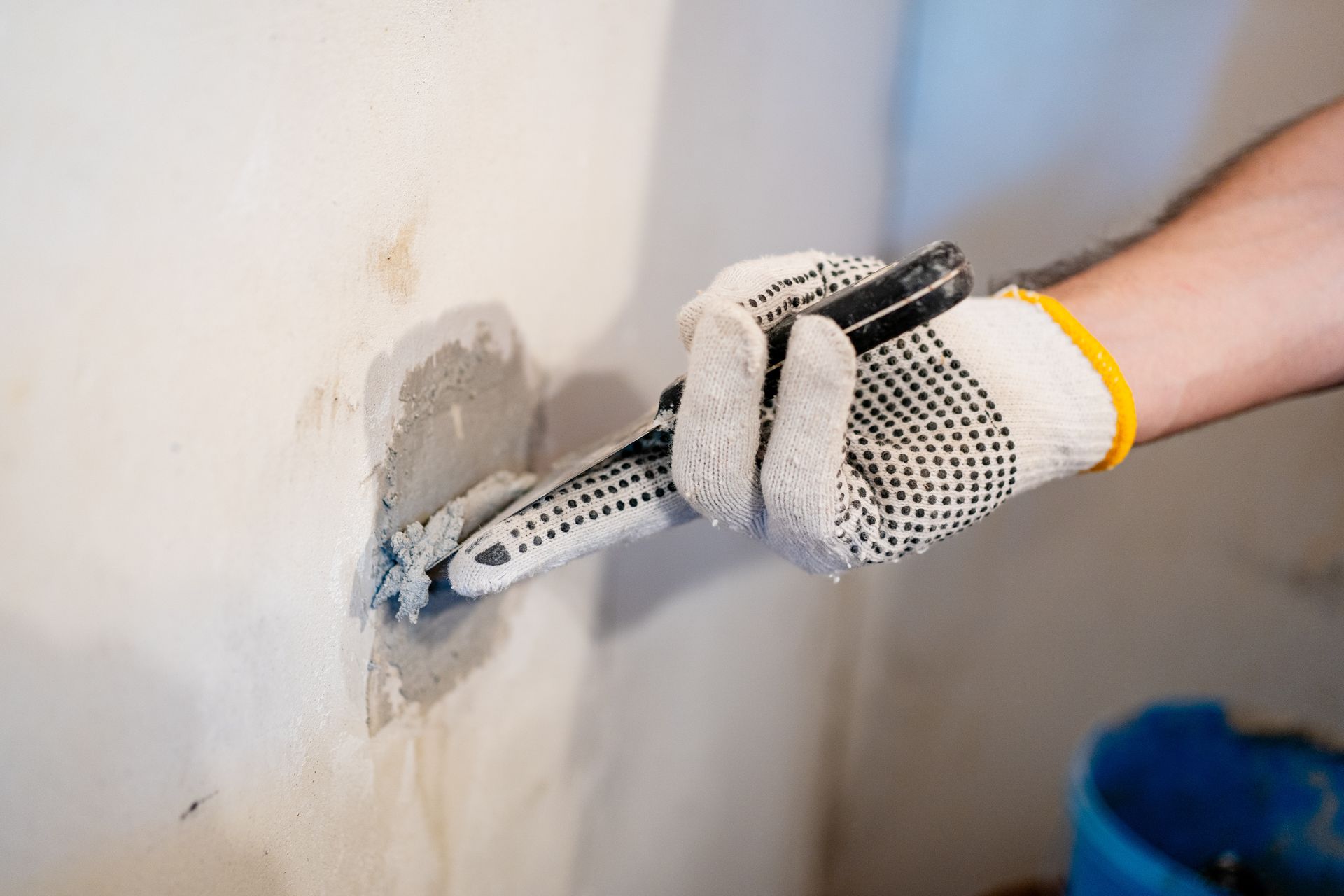 Gloved hand applying plaster to a wall with a putty knife