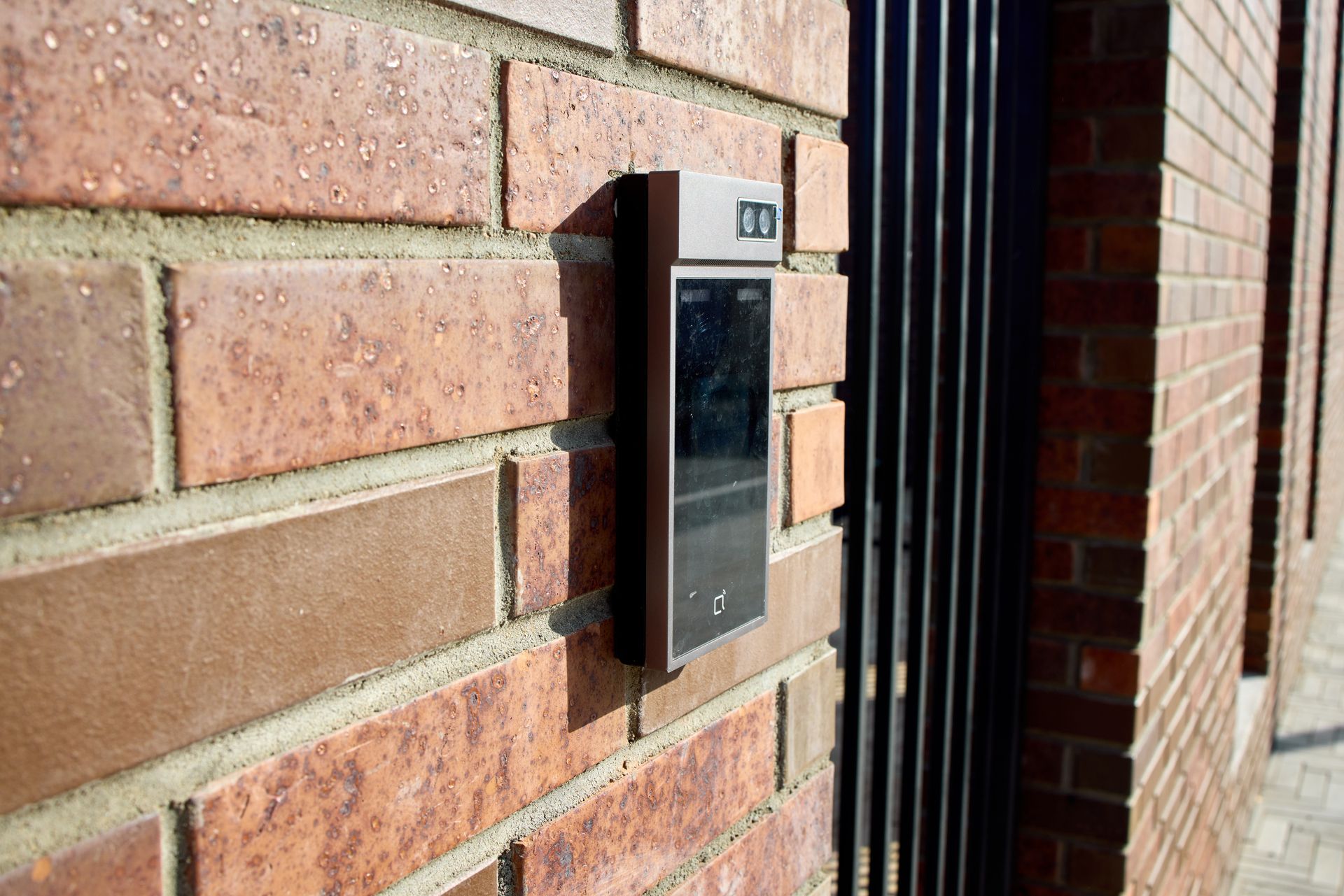 Wall-mounted black intercom keypad on a brick exterior wall by a doorway