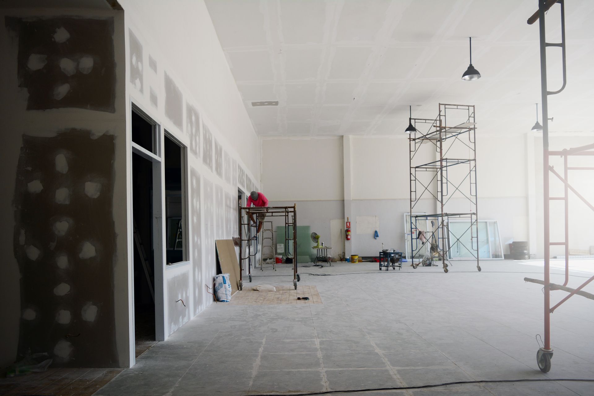 Empty indoor construction site with drywall, scaffolding, and tools on a dusty floor
