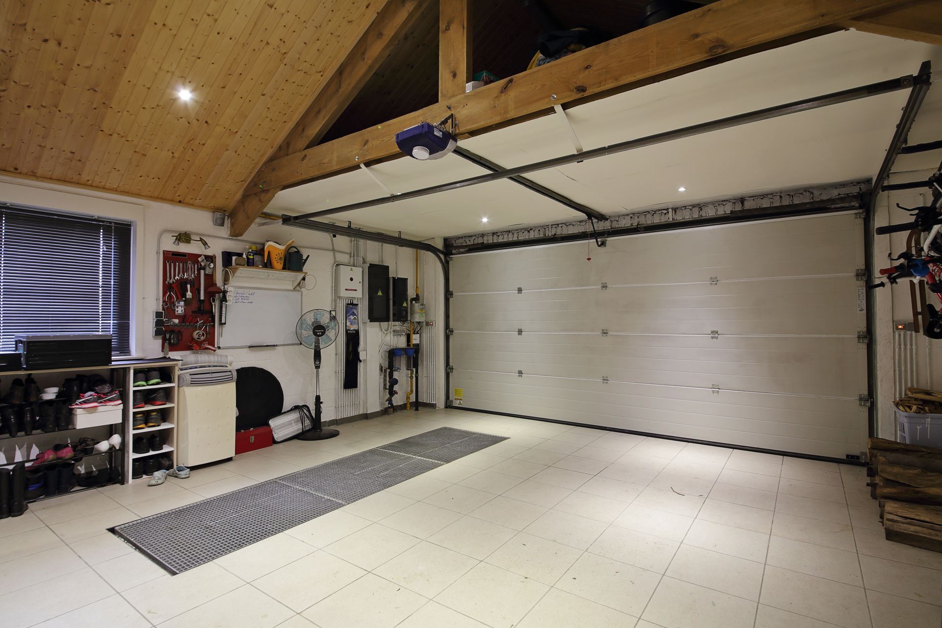 Spacious garage with white sectional door, tiled floor, shelves, and high wood ceiling open to the left