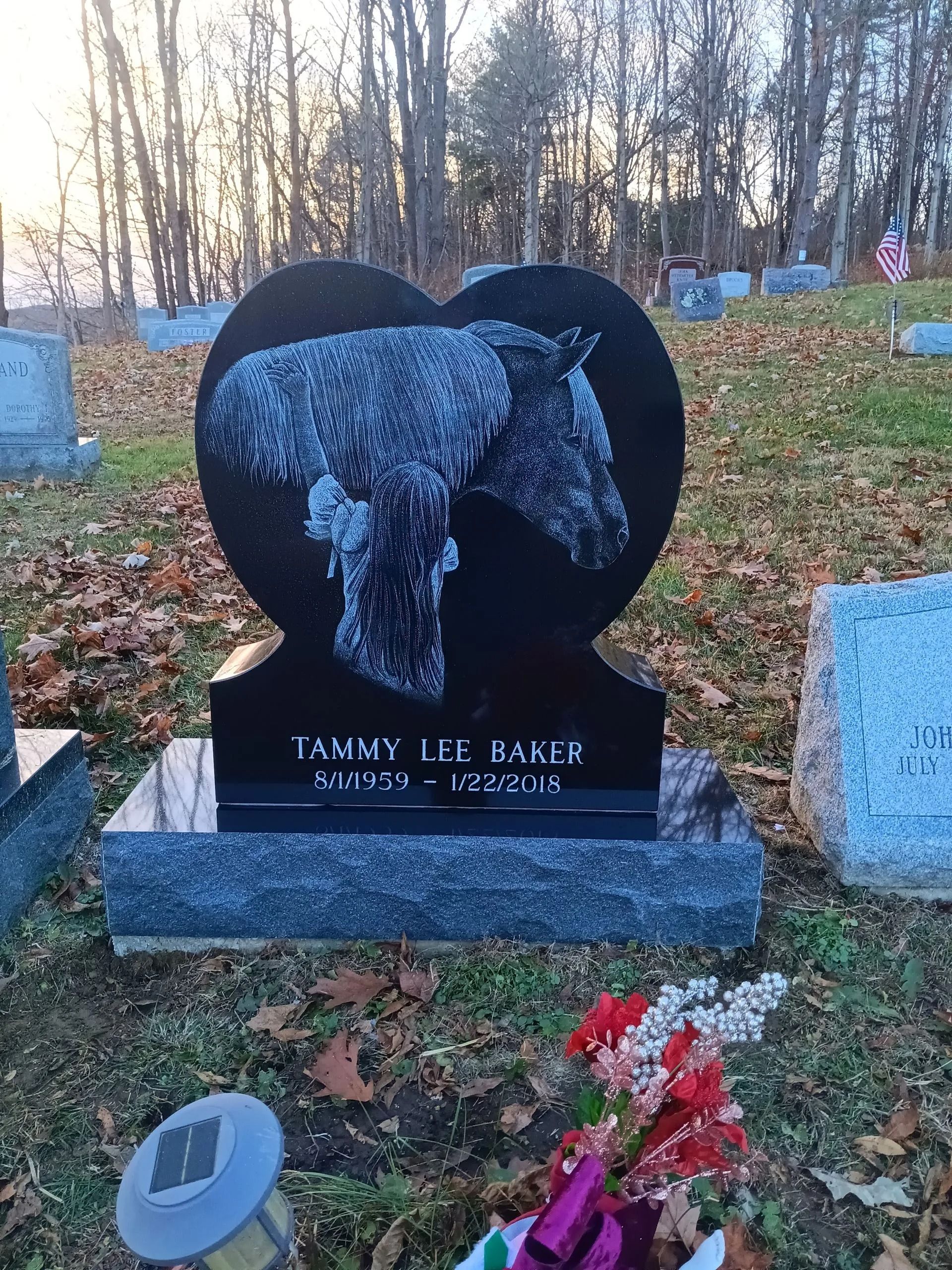 Black heart-shaped tombstone with horse etching, name Tammy Lee Harris, and floral arrangement at a cemetery.