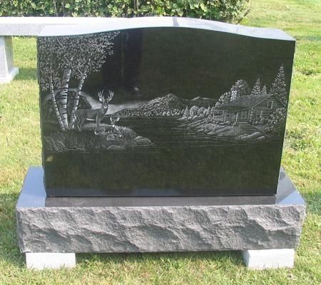 Black granite headstone with lake scene engraving, deer, cabin, and trees. Set on a gray base.