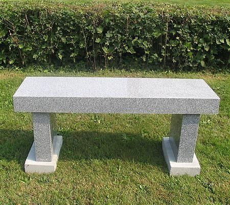 Granite bench on green grass in front of a hedge.