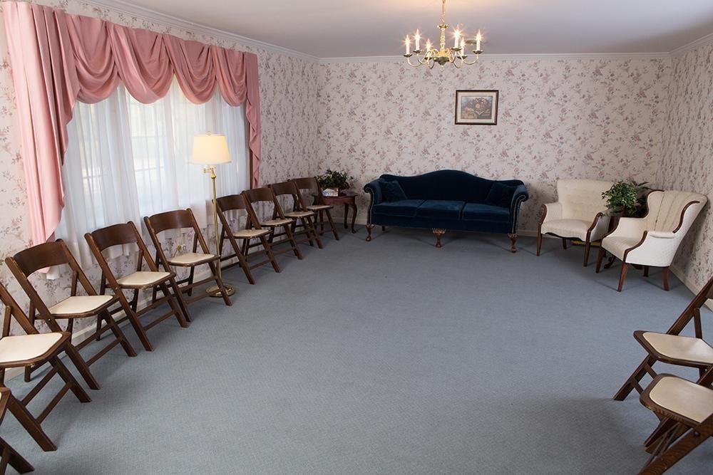 A room with folding chairs, a blue couch, floral wallpaper, and a window with pink drapes.