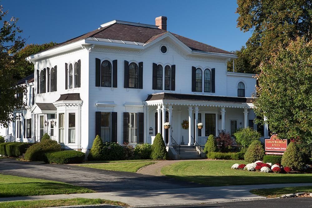 White historic building with black shutters, porch, and a well-manicured lawn.