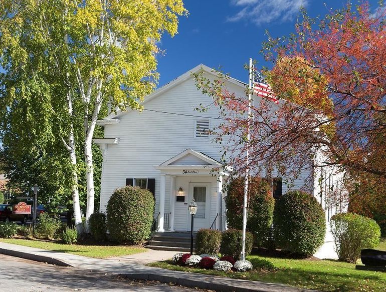 White building with American flag; trees in fall colors and bushes in front.