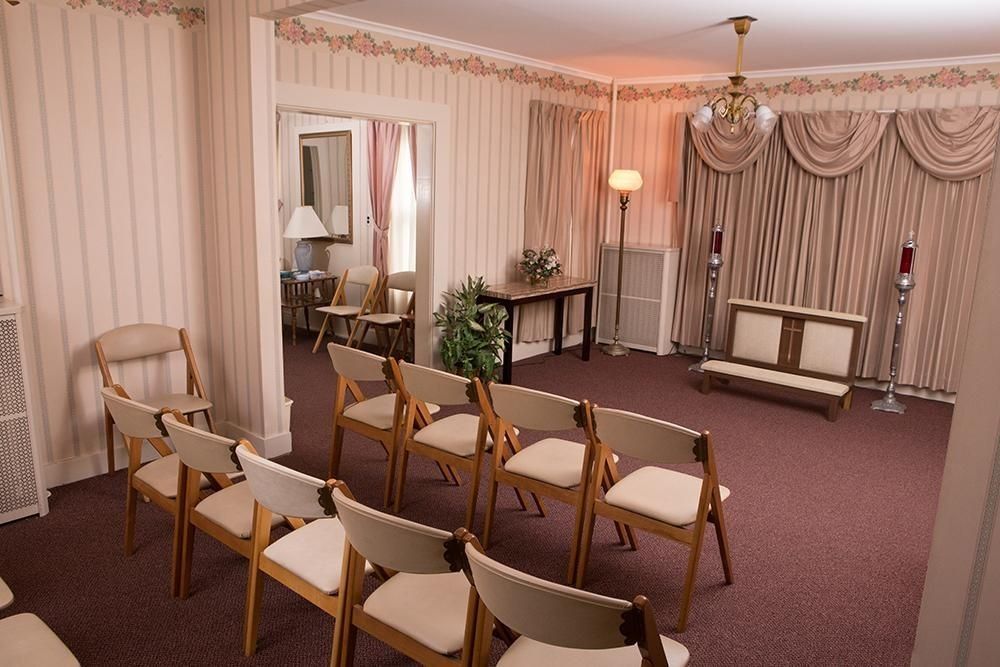 A funeral home chapel with rows of chairs, curtains, and a bench.