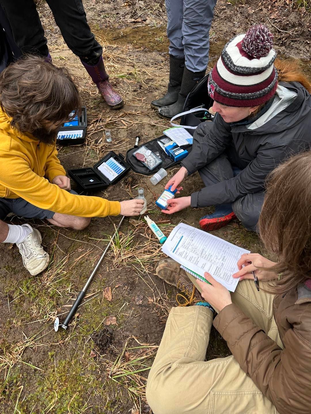 Group of people outdoors testing water. They are examining equipment and taking notes.
