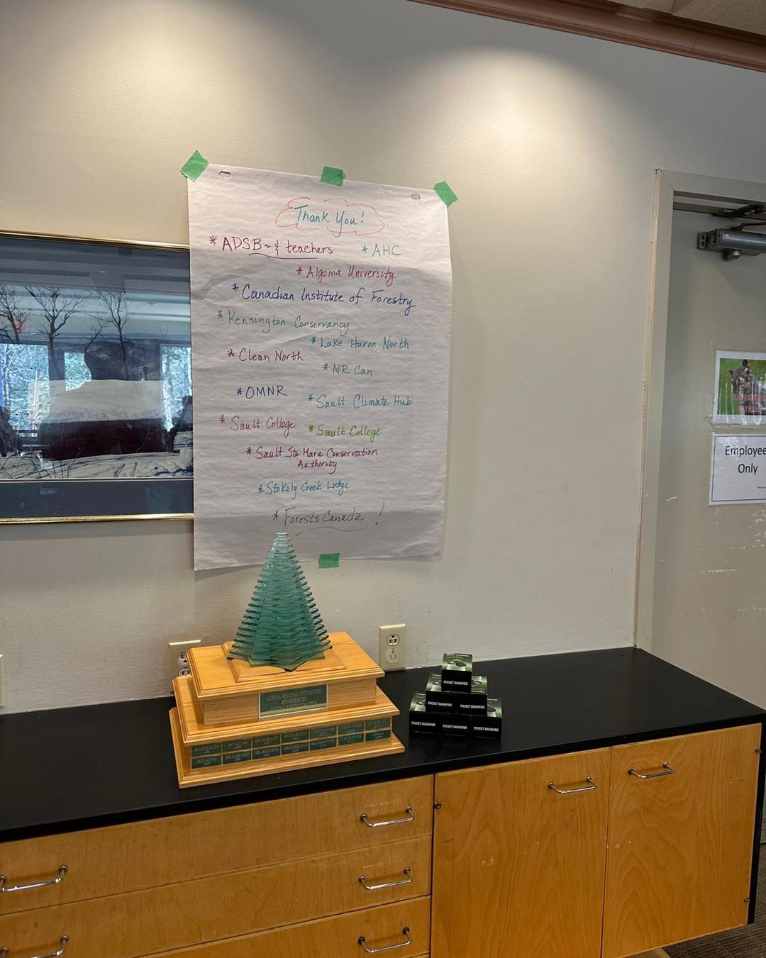 A list on a white paper taped to a wall. A desk has wooden decorations with a green pyramid.