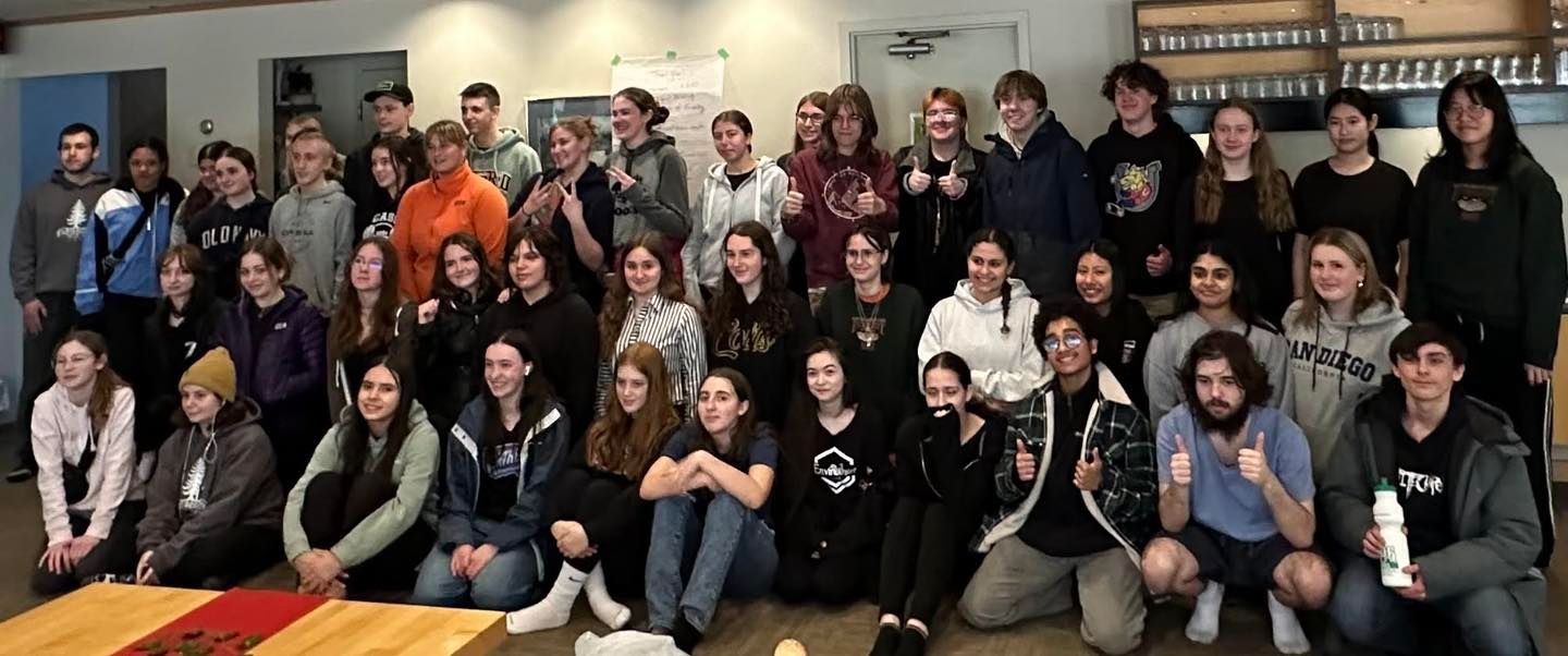 A group of students smiling and giving a thumbs-up in a room.