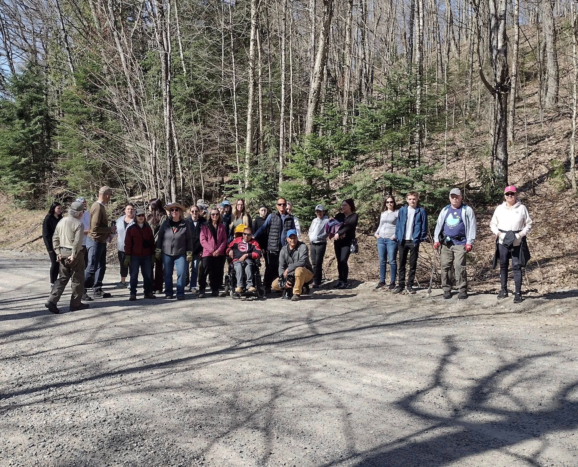 Group of people standing on a dirt path in a wooded area. Sunny day. Trees in the background.
