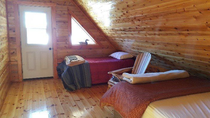 Bedroom with two twin beds, wooden walls and floors, and a small door and triangular window.