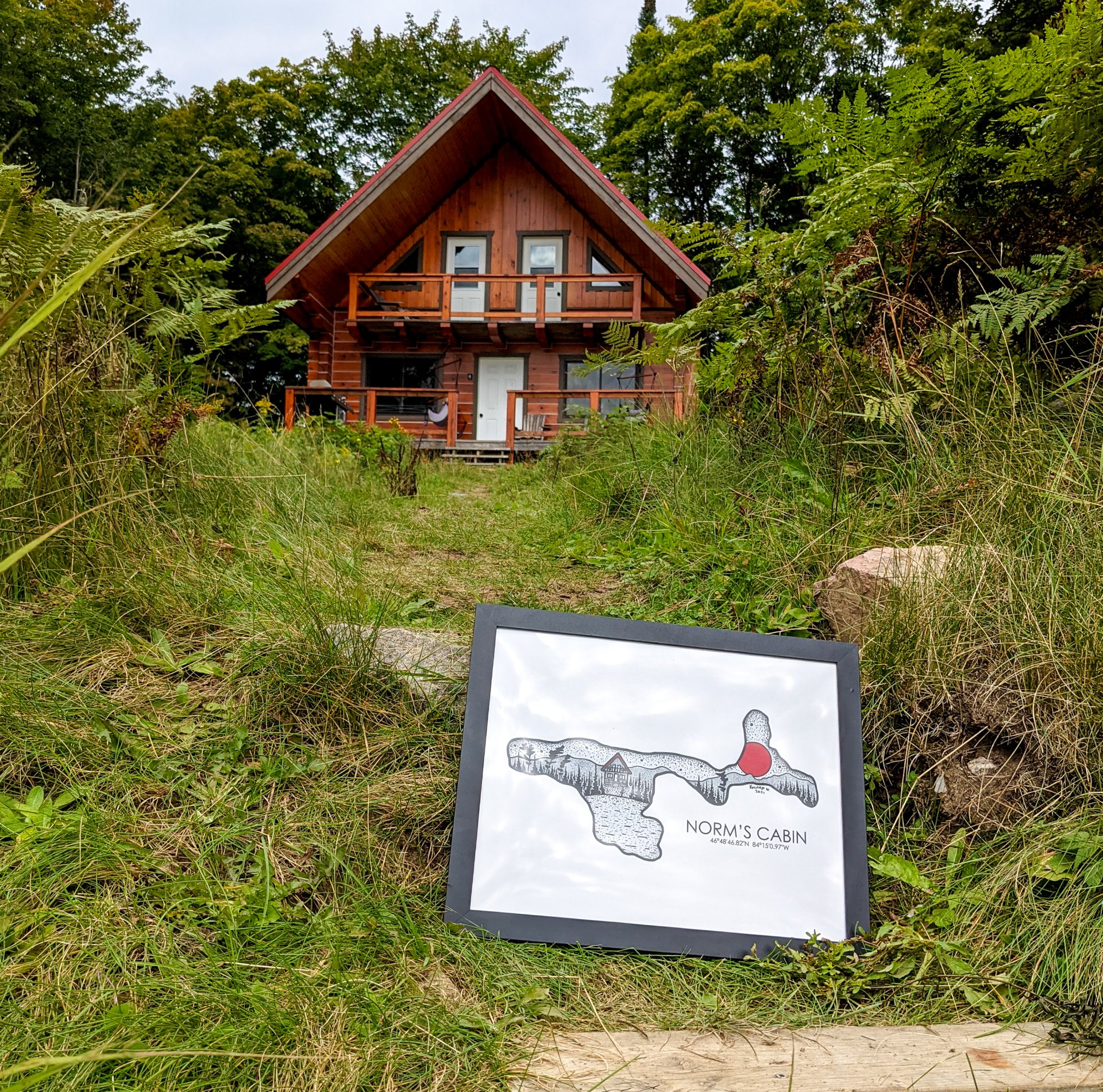A wooden cabin on a grassy hill with a trail map sign in the foreground.
