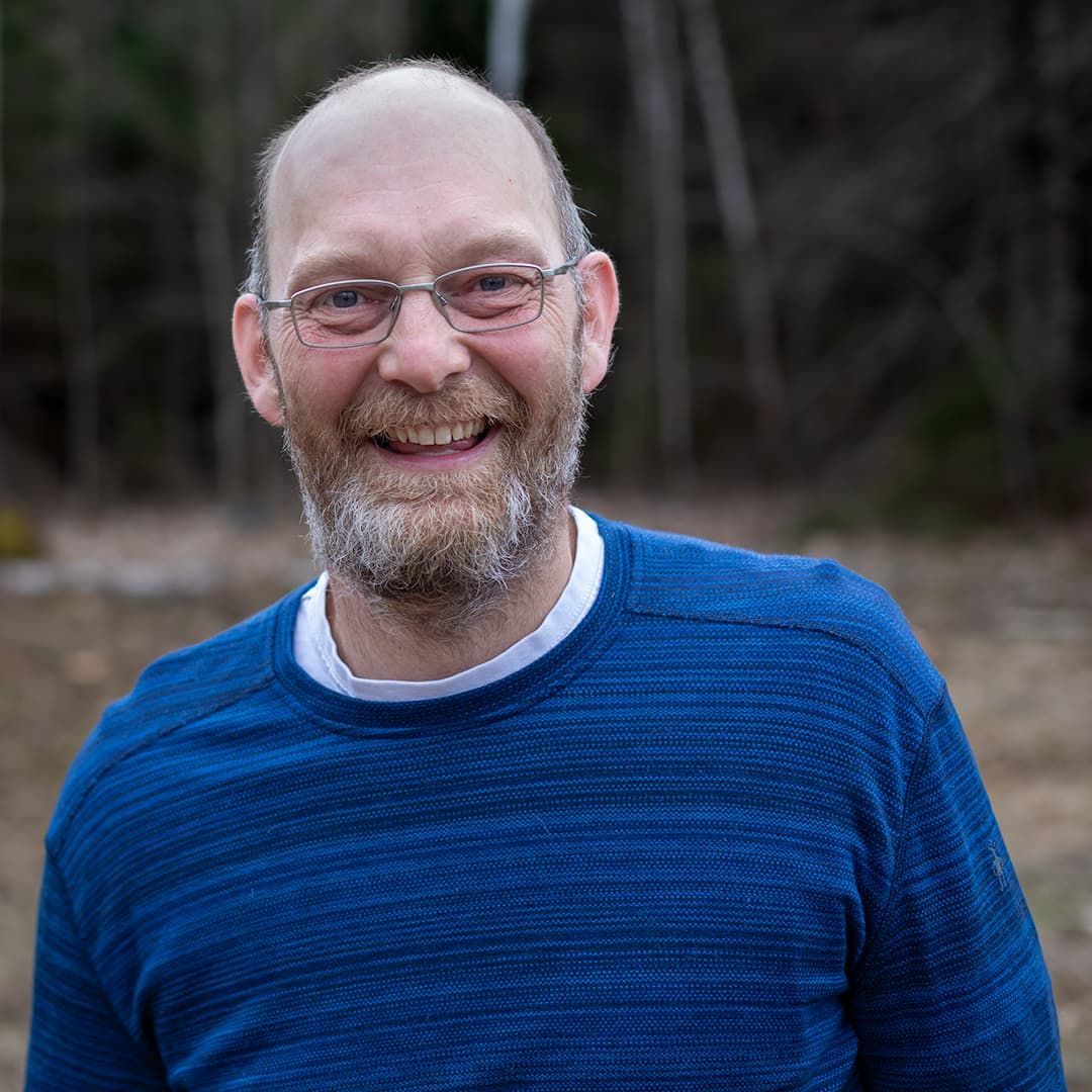 Smiling bald man with glasses and beard in a blue sweater outdoors