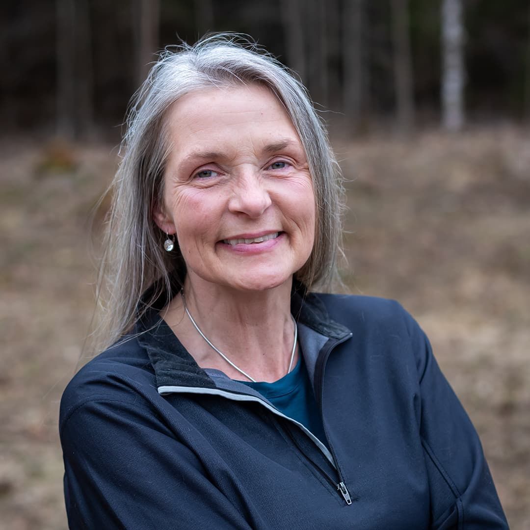 Smiling person in a navy jacket standing outdoors with blurred trees in the background