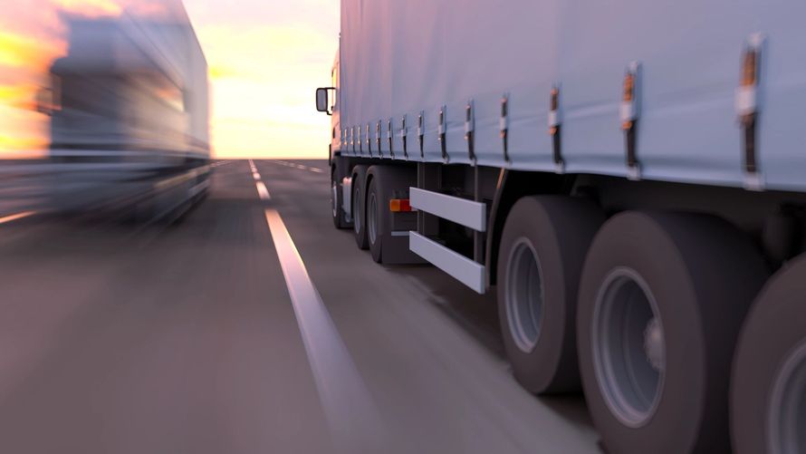 Camion sfocati che sfrecciano su un'autostrada al tramonto, con un rimorchio bianco in primo piano.