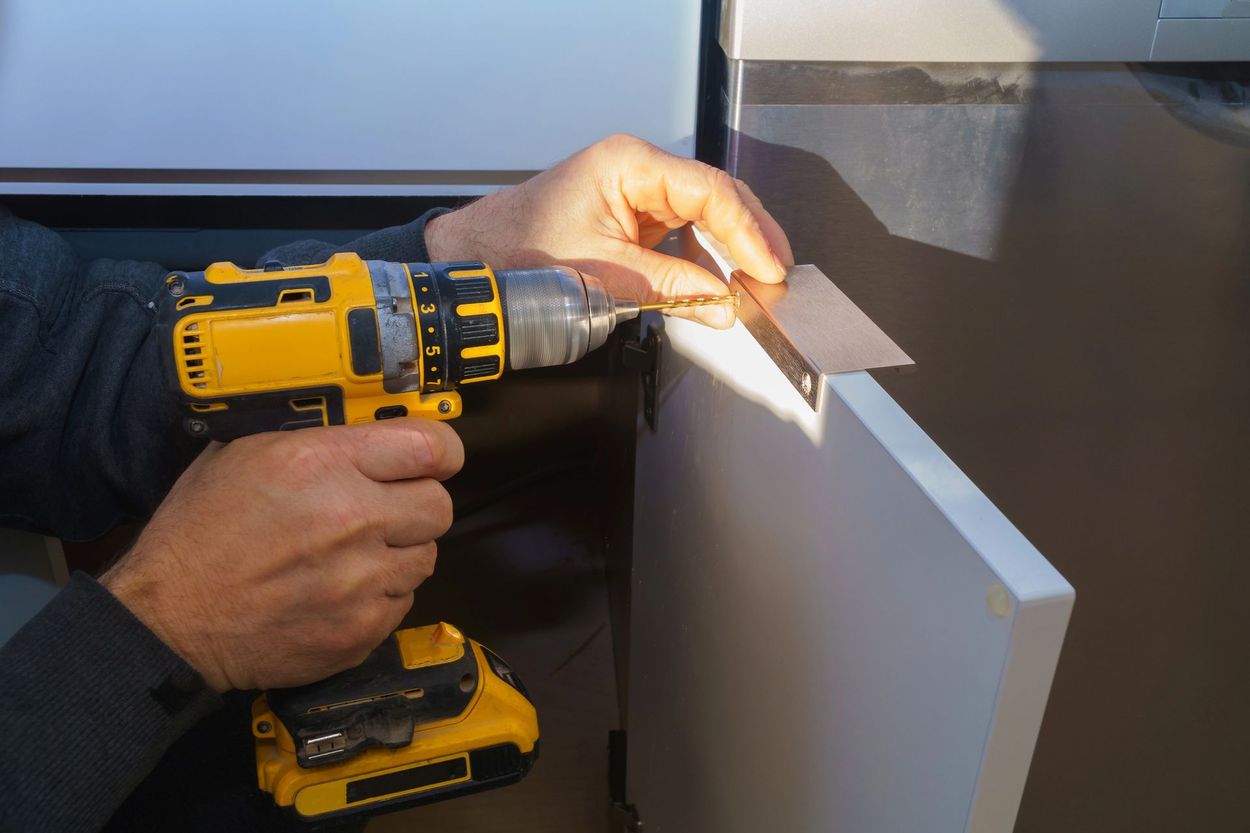 Una persona sta forando un pannello bianco con un trapano a batteria giallo vicino a una superficie metallica grigia.