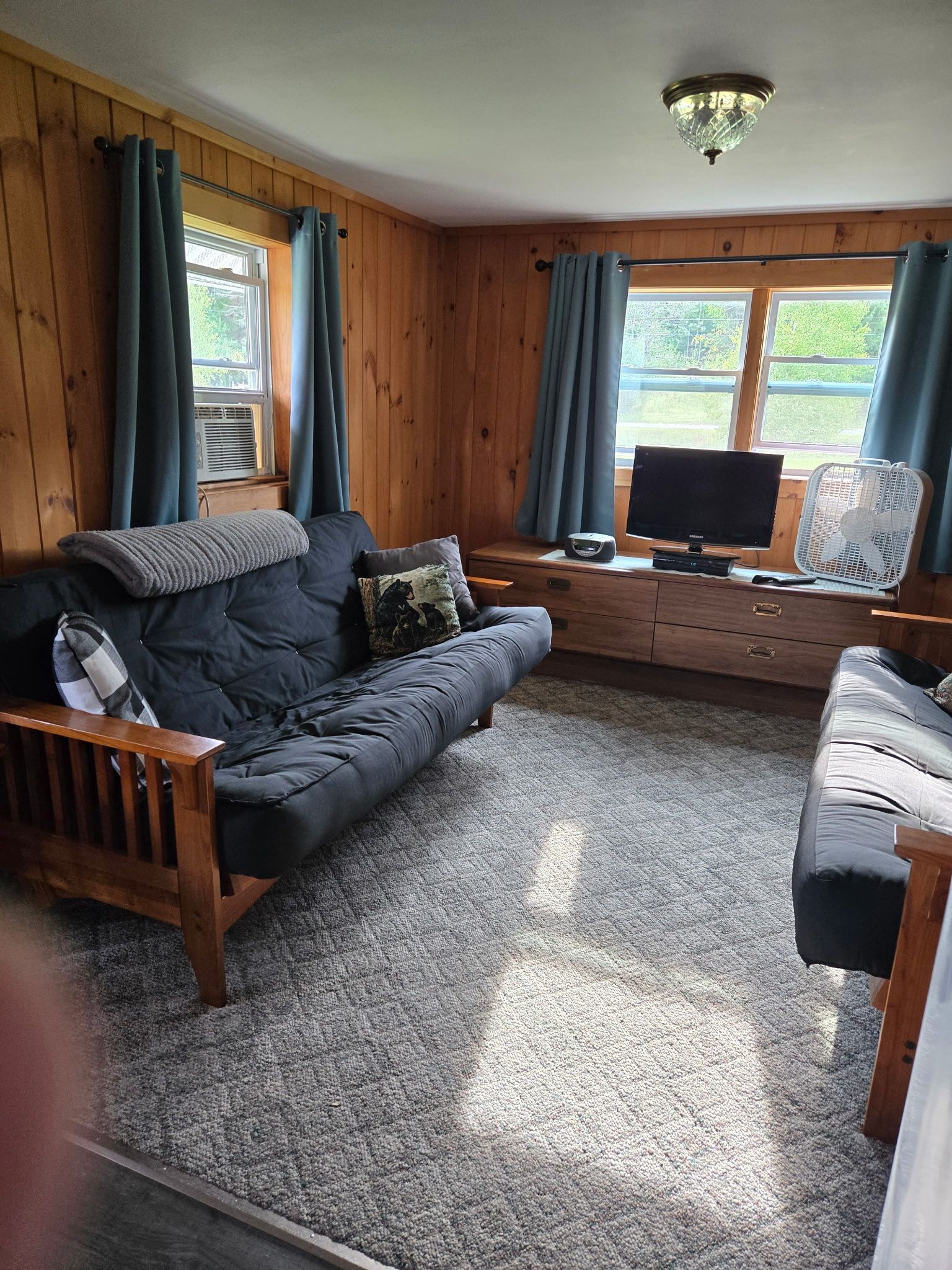 Cozy living room with gray sofas, a window seat, blue curtains, and a TV by the window.