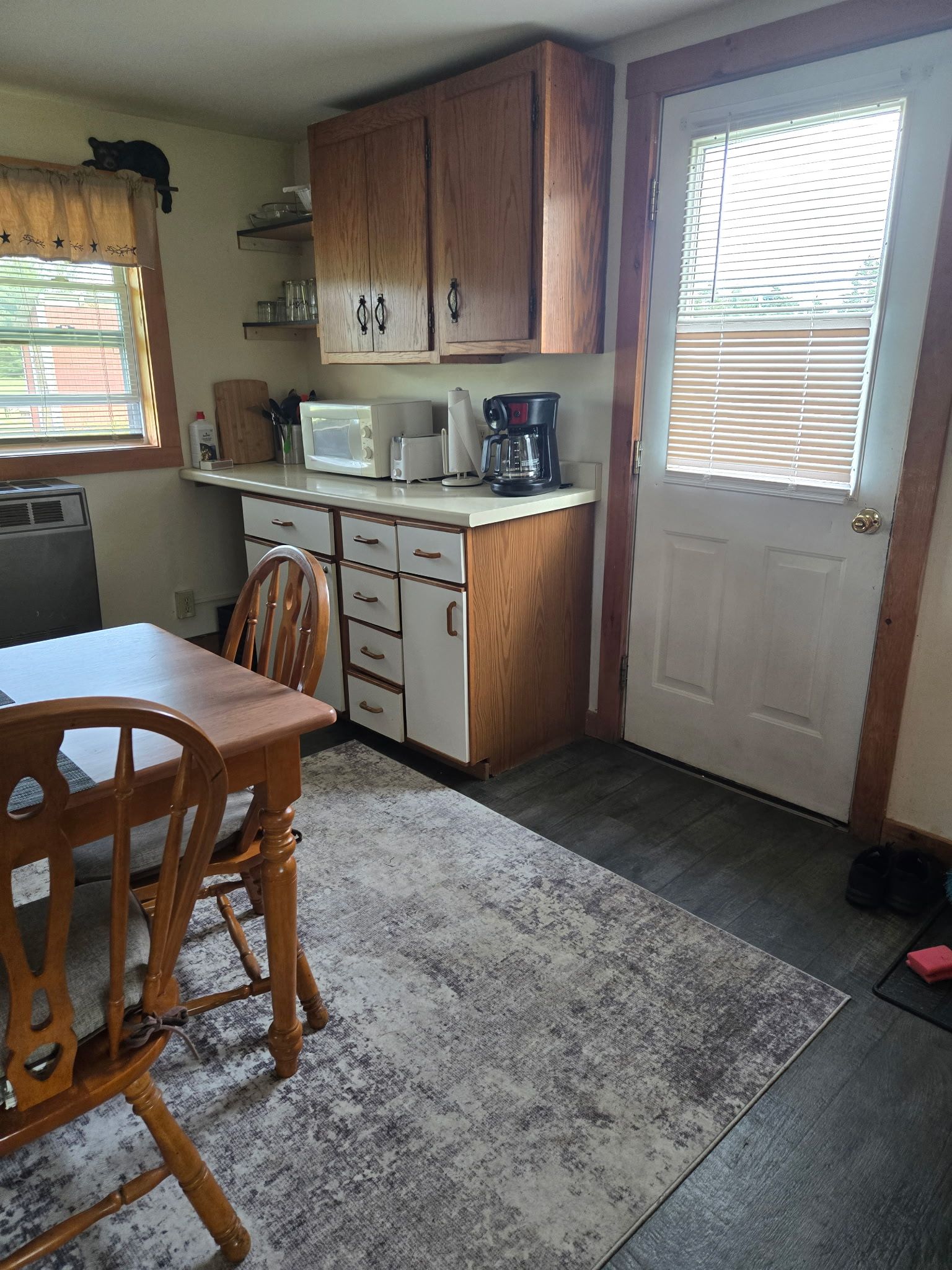 Small kitchen with wooden cabinets, white appliances, dining table, chair, and a door with blinds.