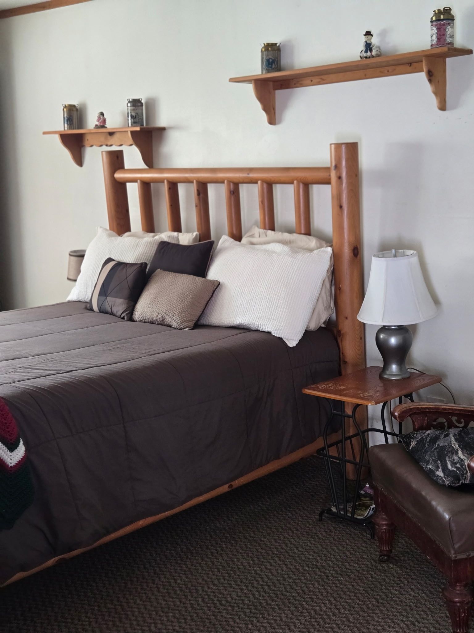 Cozy bedroom with a wooden bed, gray bedding, wall shelves, and a bedside lamp