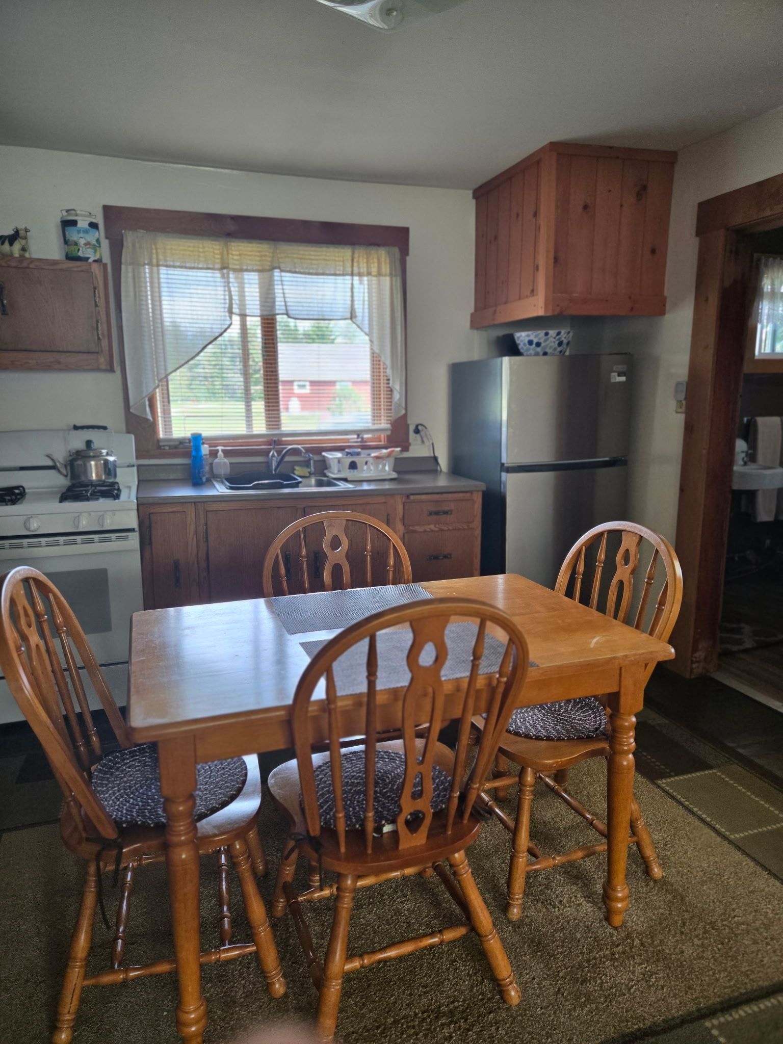 Kitchen with wooden dining table and chairs, window above sink, and stainless steel refrigerator.