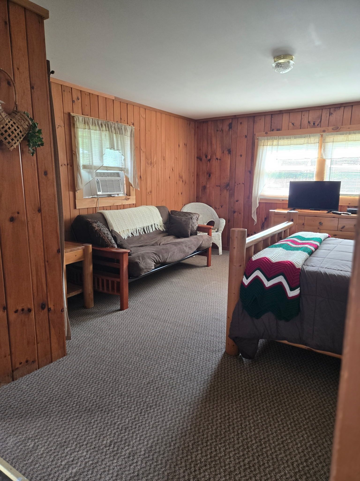 Cozy wood-paneled bedroom with twin beds, gray couch, and two windows letting in daylight