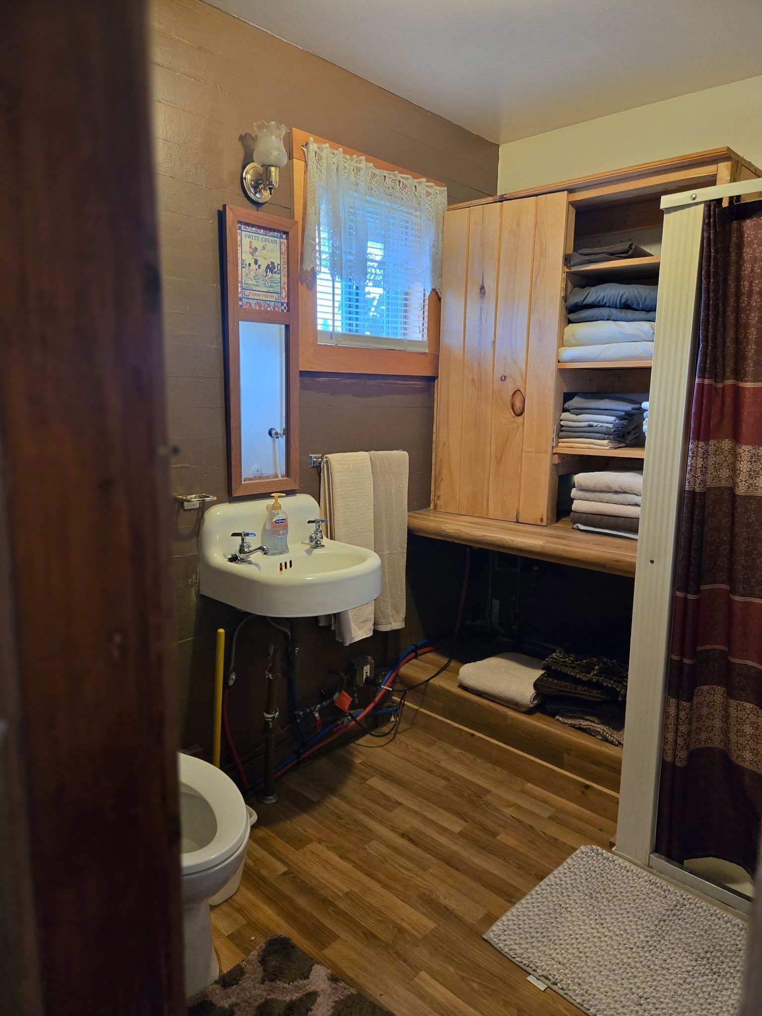 Small bathroom with sink, toilet, window, and open linen cabinet with towels and shelves